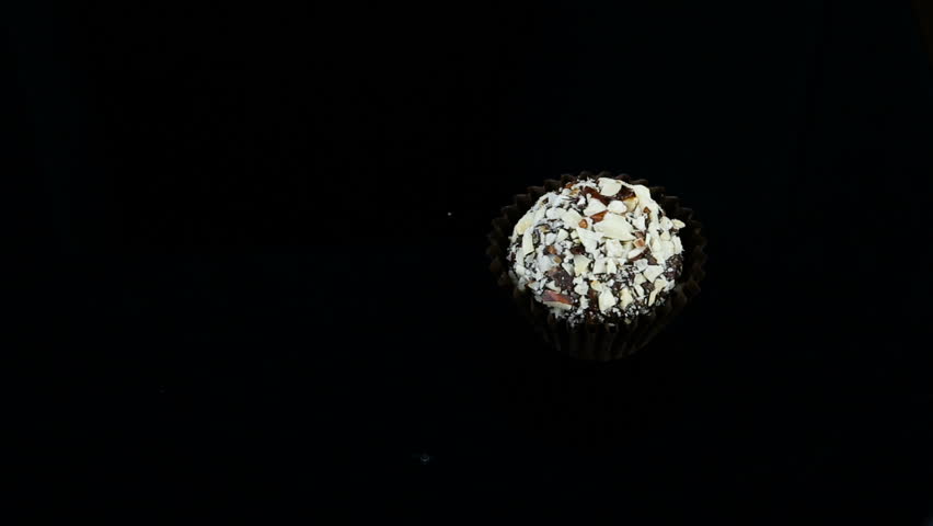 smooth panorama down on single chocolate candy decorated with crushed nuts served on black background