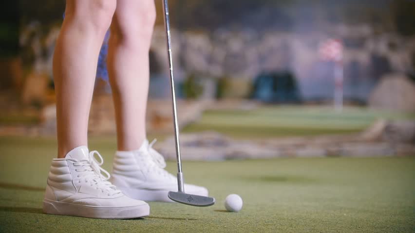 A young woman playing mini golf indoors. Legs in the frame