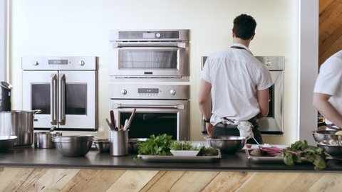 Chefs preparing to cook at their stations in interior kitchen with soft day lighting. Wide shot on 4k RED camera.