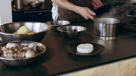 Chef taking a pot of hot, steaming water into another bowl with beets and stirs it together in interior kitchen with soft day lighting. Medium shot on 4k RED camera.