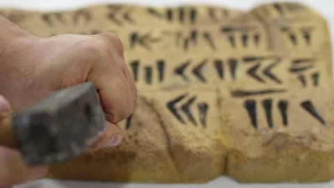 Ancient cuneiform writing by a man using a hammer and chisel