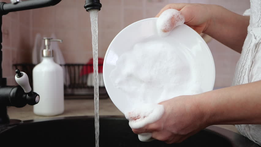 Woman hands rinse plate at the kitchen sink - doing the chores at home. Dish washing routine, static camera. | Shutterstock HD Video #1026440639
