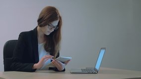 Video of a young attractive businesswoman smiling while using her tablet in front of her laptop in an office