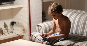 Child seated at living-room sofa holding cellphone device at home candid