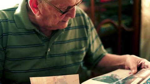 Senior man looking at photos by table at home, 4K
