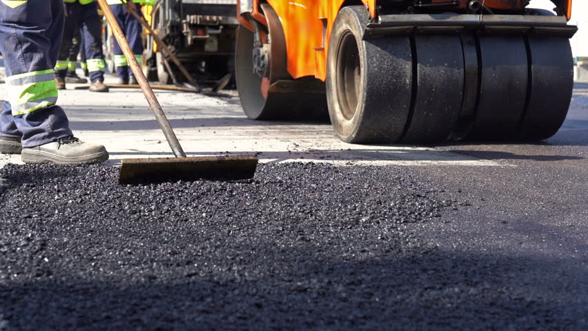 Road Construction and Repairing Works - Slow Motion. Worker Leveling Fresh Asphalt on a Road Construction Site. Worker Using Asphalt Lute. Teamwork On Road Construction. Royalty-Free Stock Footage #1026449432
