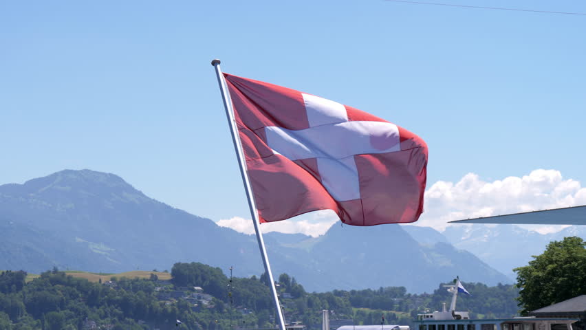 Swiss national flag on the background of the majestic Alpine mountains.