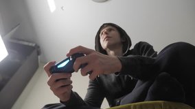 boy teenager in the hood playing video games on the console on the gamepad lifestyle . Young teen Man hooded sweater Absorbed In Online Video Game. Controller console gamepad. Gaming man holding