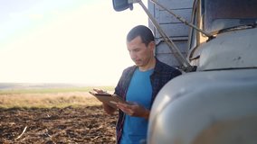 smart farming. man farmer driver stands with a digital tablet near the truck. slow motion video. Portrait businessman farmer standing in the field harvesting season car. Farmer driver uses a tablet