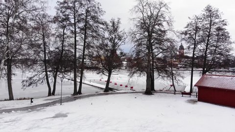 Ascending drone footage revealing a small town with a beautiful windmill the great old cathedral of Strängnäs. A frozen lake and a harbor is in the foreground. Filmed in realtime at 4k.
