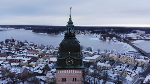 Drone footageing away from the old cathedral of Strängnäs with the old town and a frozen lake with a bridge in the background. Filmed in realtime at 4k.