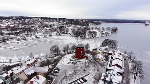 Drone footage flying over a small town towards a beautiful windmill. A frozen lake with a harbor in the background. Filmed in realtime at 4k.