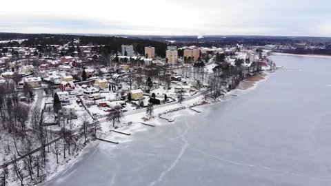Drone footage flying over a frozen lake towards some colorful apartment buildings while tilting downwards. Filmed in realtime at 4k.