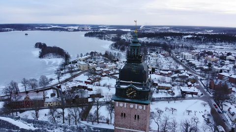 Drone footage circle around the tower of the old cathedral of Strängnäs with a frozen lake in the background. Filmed in realtime at 4k.