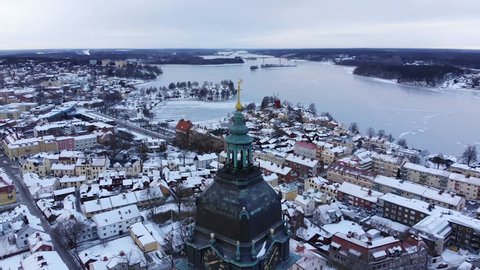 Drone footage circle around whileing away from the tower of the old cathedral of Strängnäs with the old town and a frozen lake in the background. Filmed in realtime at 4k.