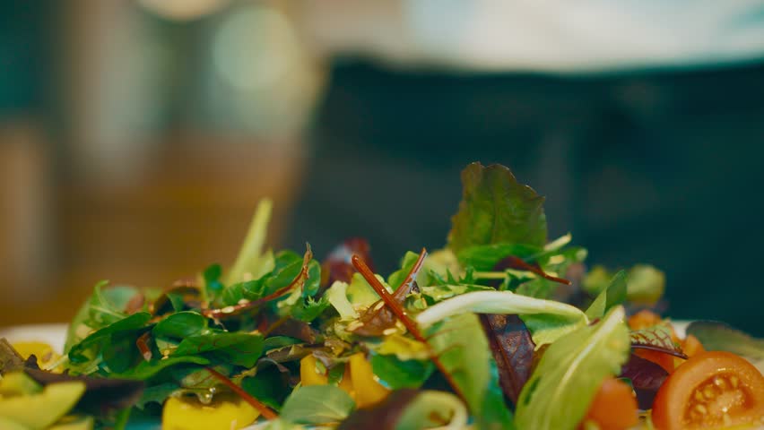 Olive oil pouring over fresh mixed salad. Close up. Cooking workshop. Finish touch to a fresh summer salad with greens, tomatoes and goat cheese. Low-calorie detox healthy food. Black apron. 