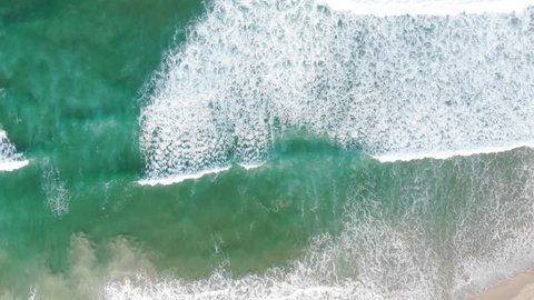 Aerial drone footage. Looking down vertically. Drone tracking breaking wave as it makes its way to the beach. Drone travelling same speed as the wave.