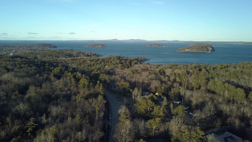 Aerial view by drone of islands in the middle of a big lake surrounded by forest with a road and a village nearby in Acadia National Park, Maine, USA