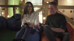 Young man and woman playing video game sitting in comfortable chairs in the cafe. Cute couple have a date and having fun together