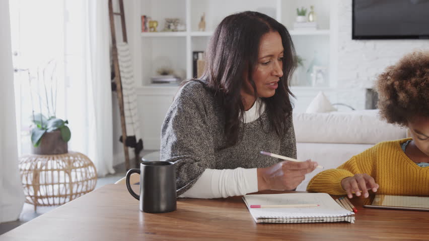 Middle aged woman sitting at the dining room table working with her granddaughter, panning shot