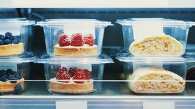 Footage of delicious desserts with berries stored in plastic containers. Food store sell bakery products from refridgerator. Enjoy sweet food for lunch