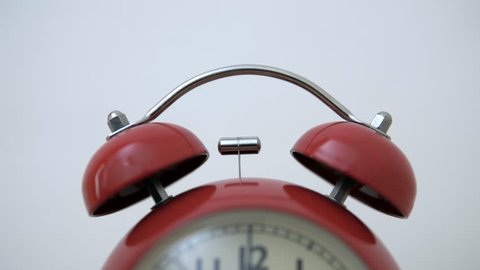 A close-up of a bell from a vintage red alarm clock that triggers the alarm.