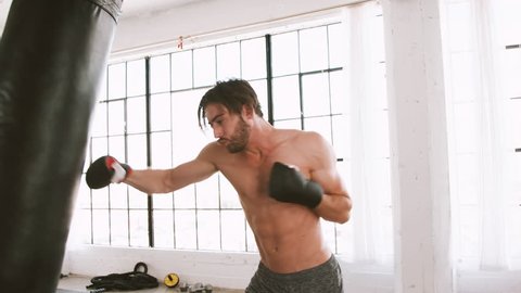 Athletic man punching a heave punching bag in a loft style gym.