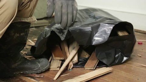 Tight Shot of a Blue Collar Worker Loading a Contractor Bag Full of Water Damaged Hard Wood Flooring.