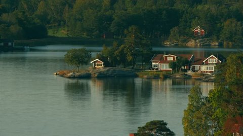 Beautiful homes and vacation cottages on the tiny islands of the Stockholm Archipelago. Calm water reflects the scene and landscape. Slow motion aerial view. Cameraing left.