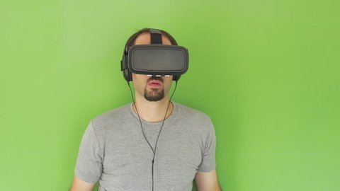 Medium shot of a Man with VR Goggles and headphones standing looking slowly on green screen