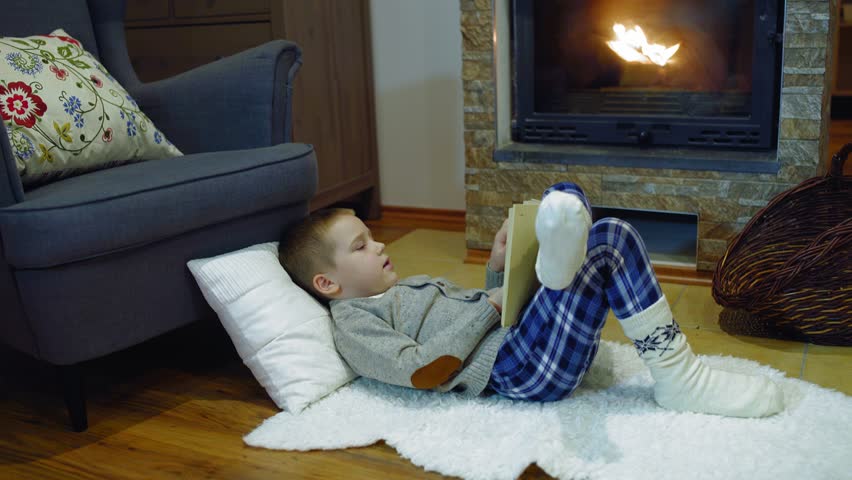 Happy child reading a book at home, near the fireplace, Christmas time