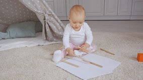 cute toddler kid sitting on fluffy carpet near baby wigwam and playing with papers and color pencils
