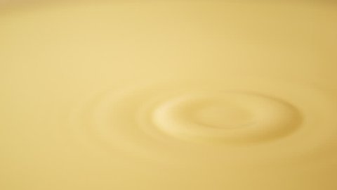 Drop of orange juice falling and making ripples, waves in slow motion filmed with high speed footage
