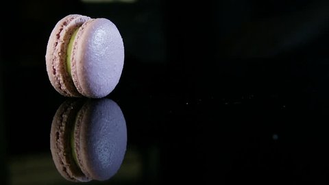human hand puts on edge three violet french dessert macaroon with green creamy filling in row on black mirror background