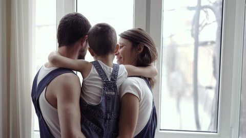 cute family standing at the window of a new home. They look out the window and rejoice, smile, hug