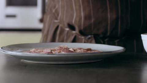 Professional focused chef carefully placing sliced red peppers on top of pieces of veal on a plate in interior kitchen with soft day lighting. Close up shot on 4k RED camera.