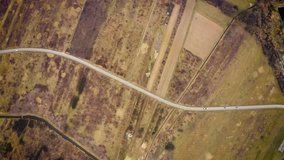 Aerial view high above car driving through dry farm land road trip flying over car on empty country road in barren landscape 4k footage of cars on road