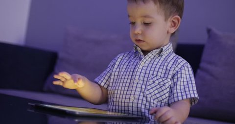 Cute Child Entertaining With Tablet. Little Boy Spending Leisure Time Playing Mobile Game in the and Crushes the Bright Screen With Her Hand. Concept of:Happy Childfood, Technology, Childen Play Games