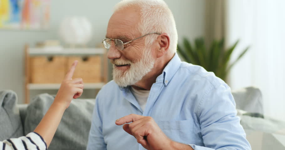 Close up of the happy grandpa and his teenage granddaughter playing and smiling while sitting on the couch in the cozy living room and man touching her nose. | Shutterstock HD Video #1026526460