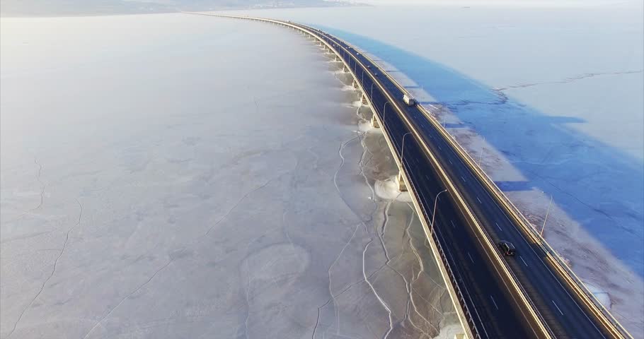 Flying above low water bridge across frozen Amur bay. Aerial veiw of cars driving fast along the road in the morning. Far East of Russia