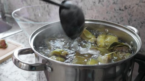 Boiling and cooking artichokes in saucepan, closeup in kitchen
