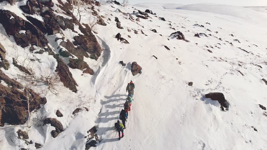 seven travelers are in one line up to the peak of a snow covered hill, in a way it helps their gear and backpacks with supplies