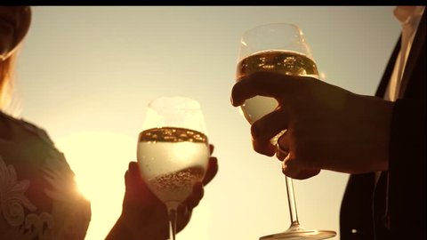 champagne sparkles and foams in sun. couple in love holding wine glasses with sparkling wine on background of sunset. closeup. teamwork of loving couple. celebrating success and victory. Slow motion