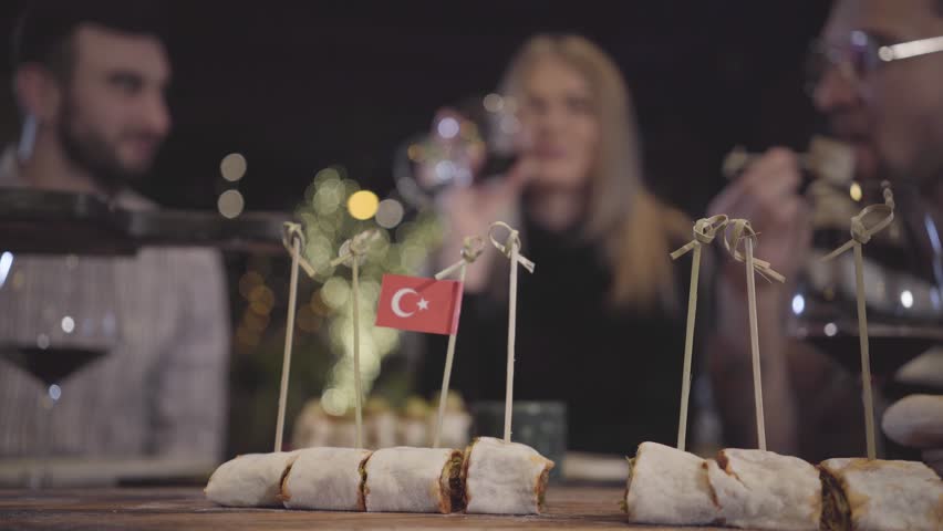 Two men and woman clinking their glases with red wine sitting at the table in modern turkish restaurant. Young people ordered lot of tasty baked food. Friends have meeting, relaxing together