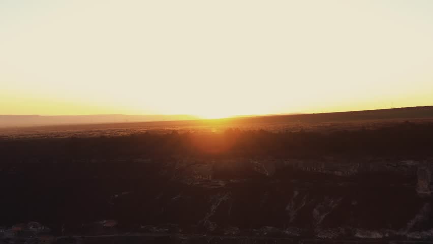 Large panorama of beautiful highlands. Orange field and horizon. Lens flare. Relax tourist. Drone up height of air on stony sheer cliffs bright late sunset on sunny day in spring Aerial view
