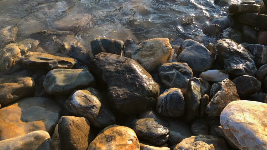 A close up shot of a rocky pebble river shoreline revealing a beautful sunset over the mountains in the far distance
