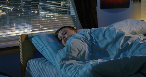 Medium shot of a boy looking out window while lying in bed and trying to fall asleep