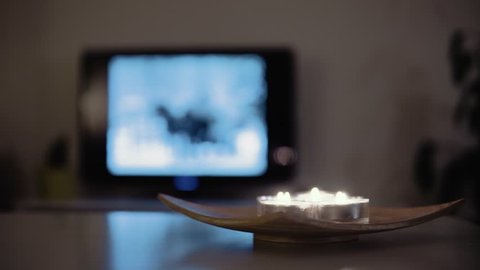 4K stationary shot of multiple tealight candles being blown out on wooden board. Blue smoke. Winter mood with a television in background.