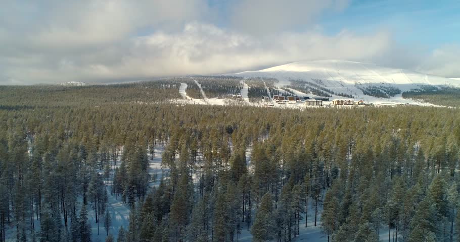 Ski resort, C4k aerial, tracking, drone shot, of Yllastunturi fell and Yllas ski center, over huts and snowy, arctic woodlands, on a sunny, winter day, at Yllasjarvi, in Muonio, Lapland, Finland