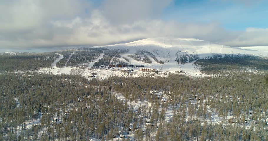 Ski resort, C4k aerial, tracking, drone shot, of Yllastunturi fell and Yllas ski center, over huts and snowy, arctic woodlands, on a sunny, winter day, at Yllasjarvi, in Muonio, Lapland, Finland